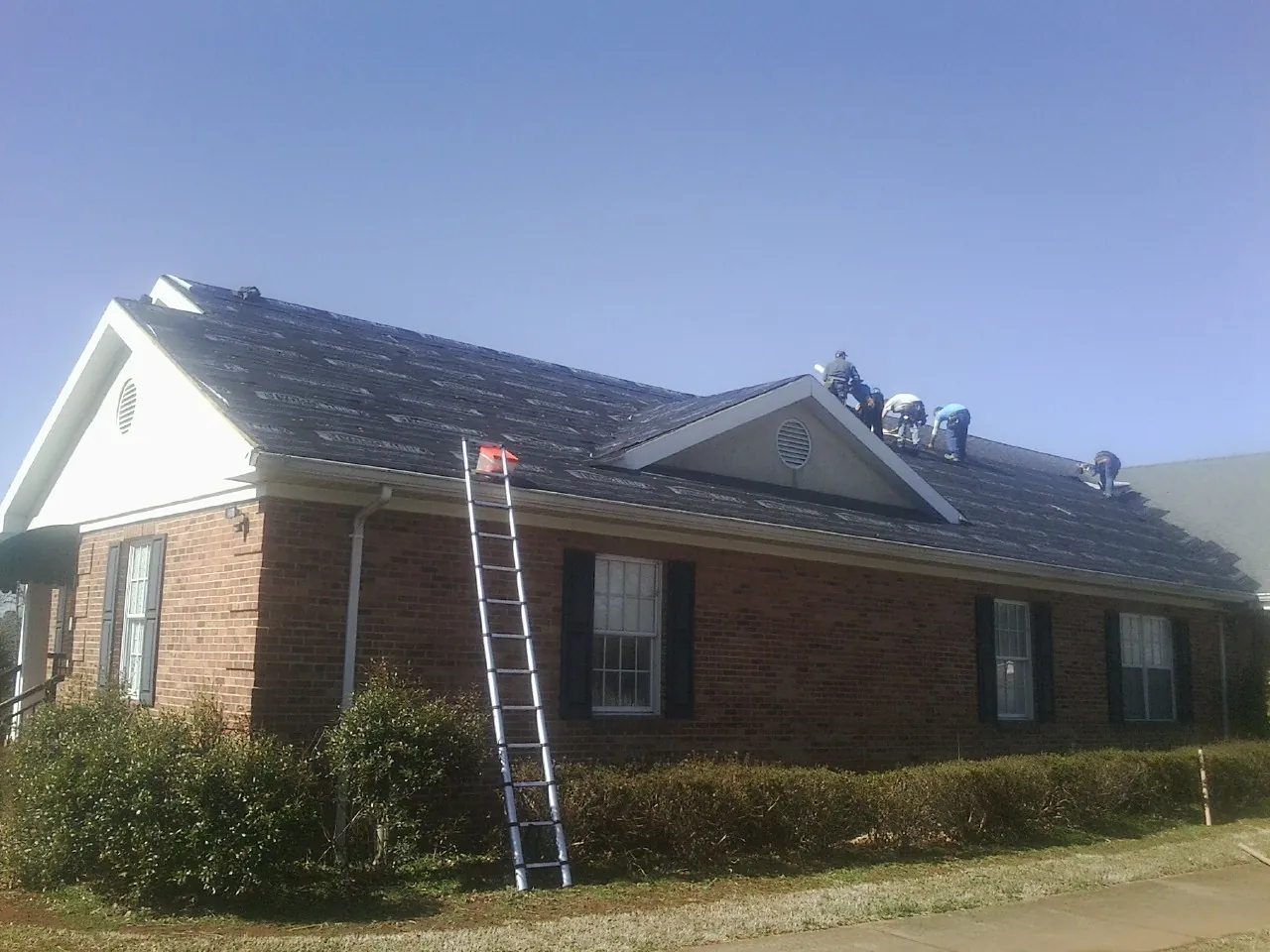 Crew tearing shingles off a brick ranch roof with a ladder set — Emergency Roof Repair work by our crew in Pioneer