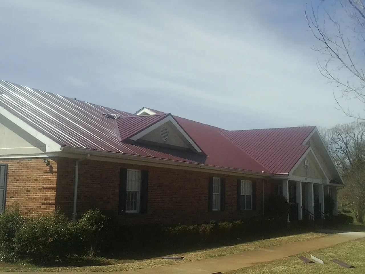 Red metal roof with gabled entries on a long brick building, from a Hail Damage Roof Repair job in Pioneer