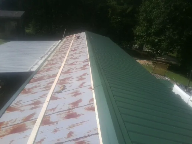 Old rusted panels beside newly installed green metal roofing — Wind Damage Roof Repair by Roofing Brothers in Pioneer
